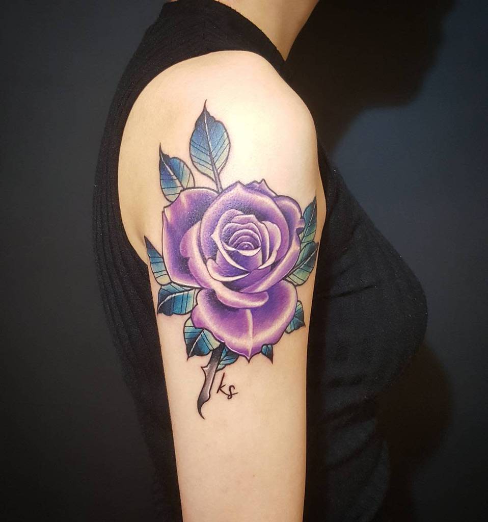 Tattoo of a large purple rose with green leaves on an upper arm
