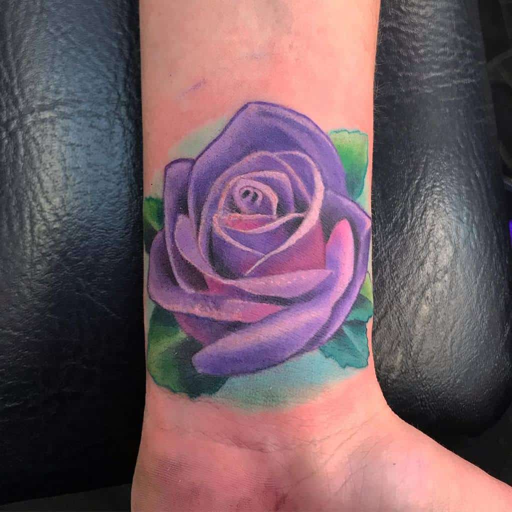 Purple rose tattoo on a wrist with green leaves
