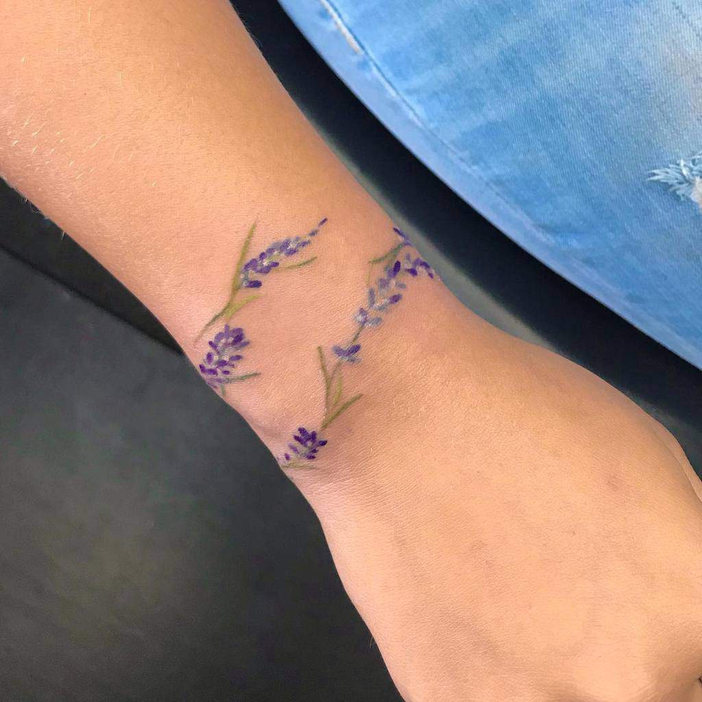 Wrist tattoo of small purple flowers and green leaves