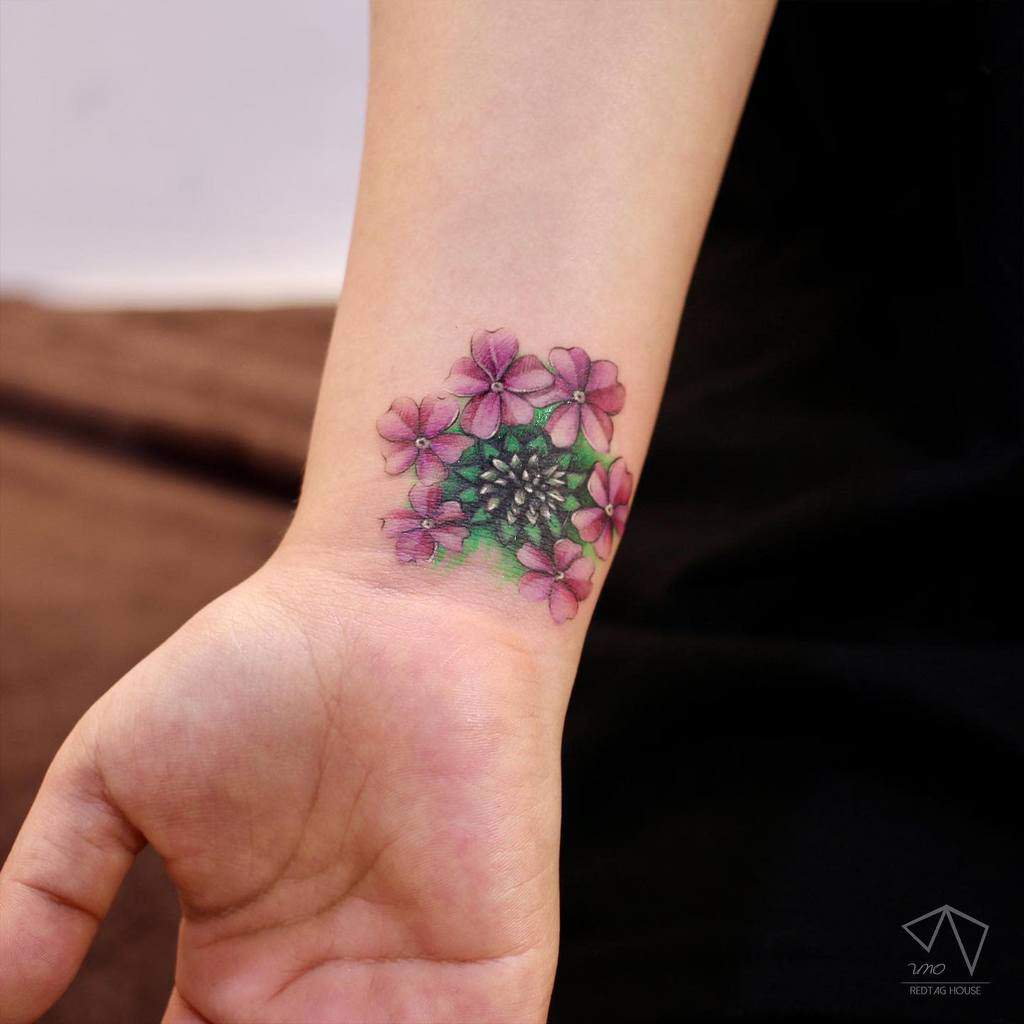 Wrist tattoo of purple flowers with green leaves