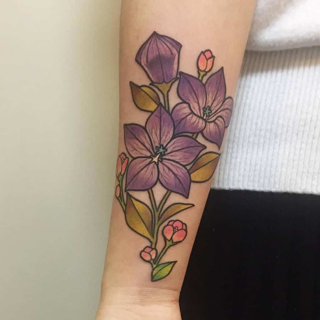 Colorful forearm tattoo featuring purple flowers with green leaves and small pink buds, outlined with bold lines