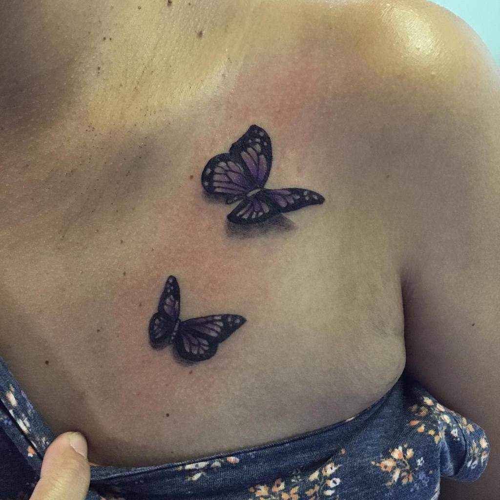 Tattoo of two purple butterflies on a person's upper chest, near the shoulder