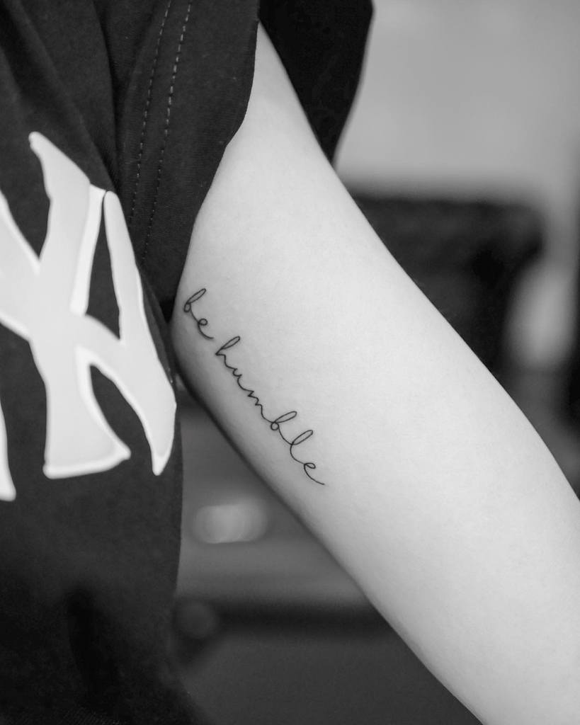Black and white image of a "be humble" tattoo on a woman's arm near the elbow