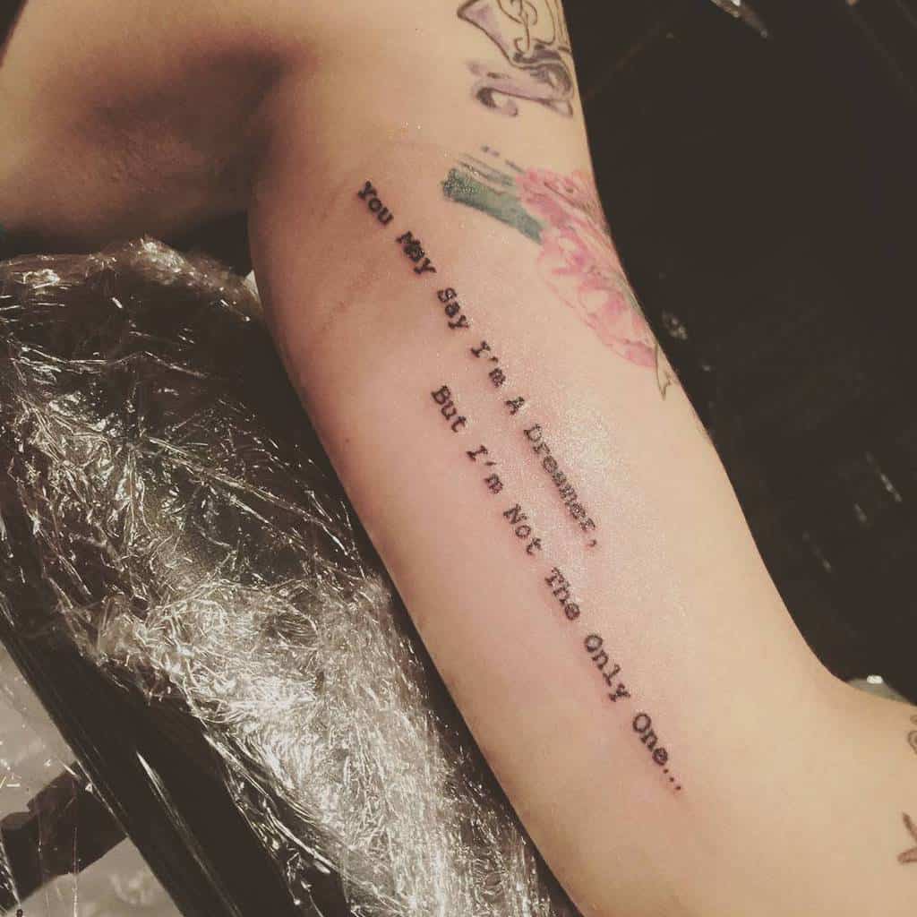 Arm tattoo with text: "You may say I'm a dreamer, but I'm not the only one" on a woman's forearm