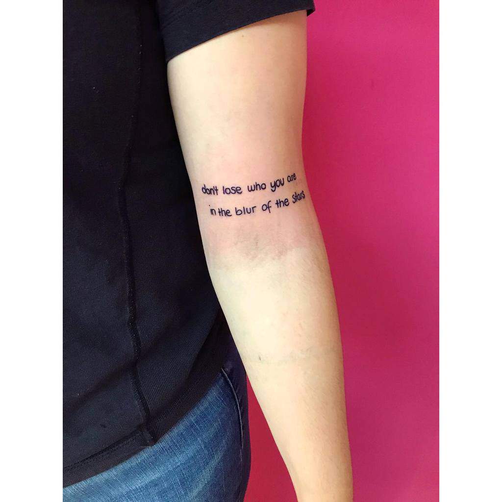 A forearm tattoo featuring the text "don't lose who you are in the blur of the star"