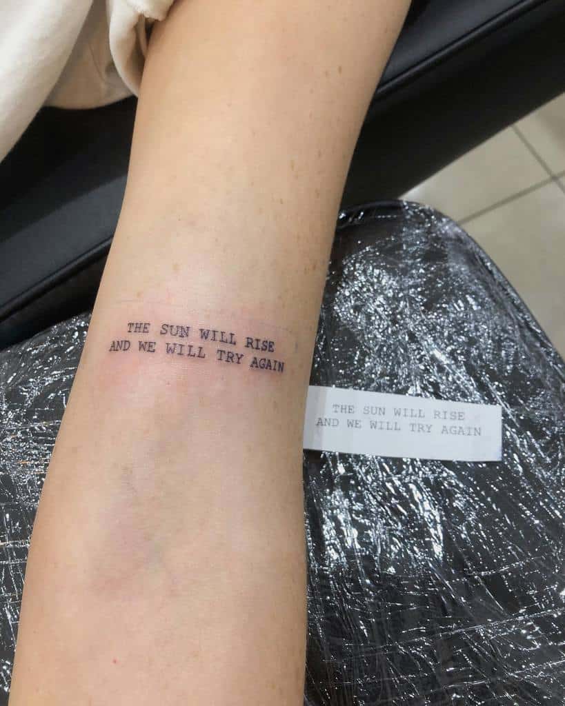 Forearm tattoo with the text "THE SUN WILL RISE AND WE WILL TRY AGAIN"