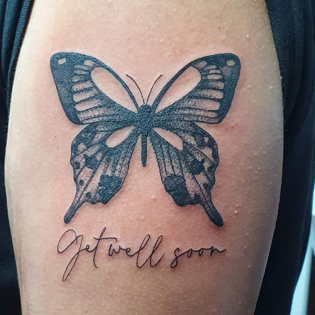Tattoo of a butterfly above the words "get well soon" on an upper arm