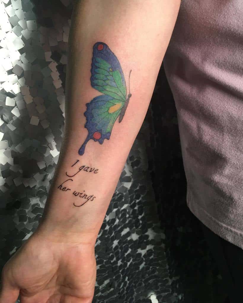 Forearm tattoo of a colorful butterfly above text that reads, "I gave her wings"