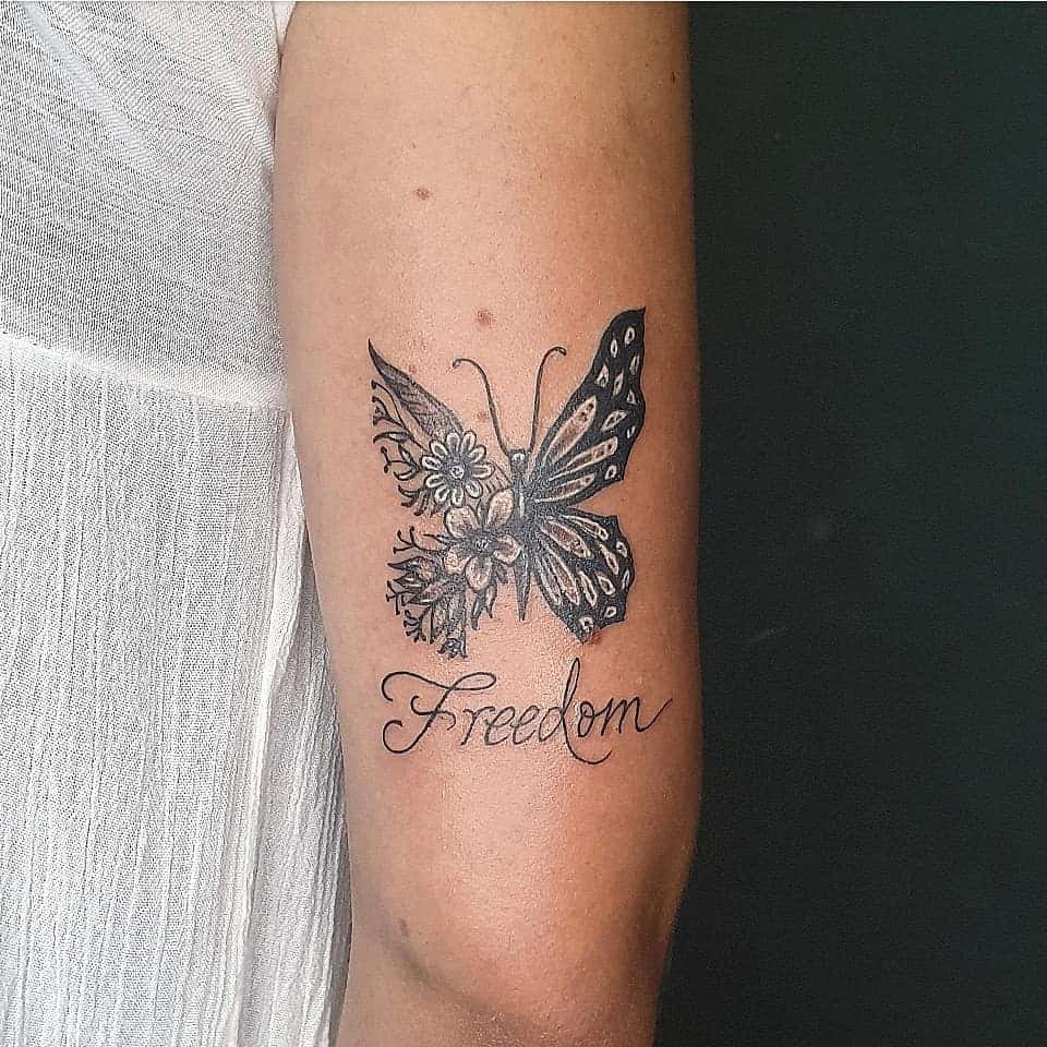 Butterfly tattoo with floral patterns and "Freedom" text on a person's upper arm