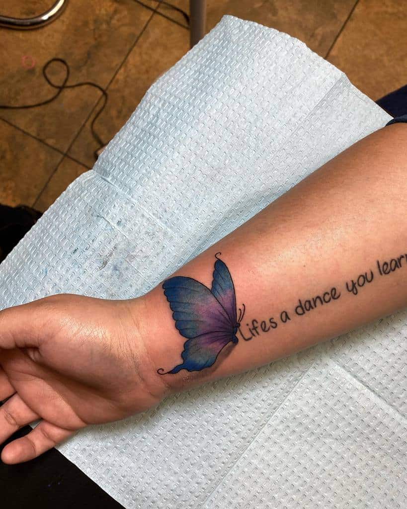 Forearm tattoo of a blue butterfly and the text "Life's a dance you learn as you go"
