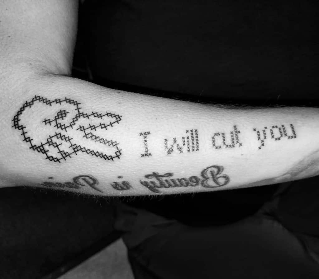 Cross-stitch style tattoo of scissors with the phrase 'I will cut you' in pixelated embroidery font, creating a playful and edgy design