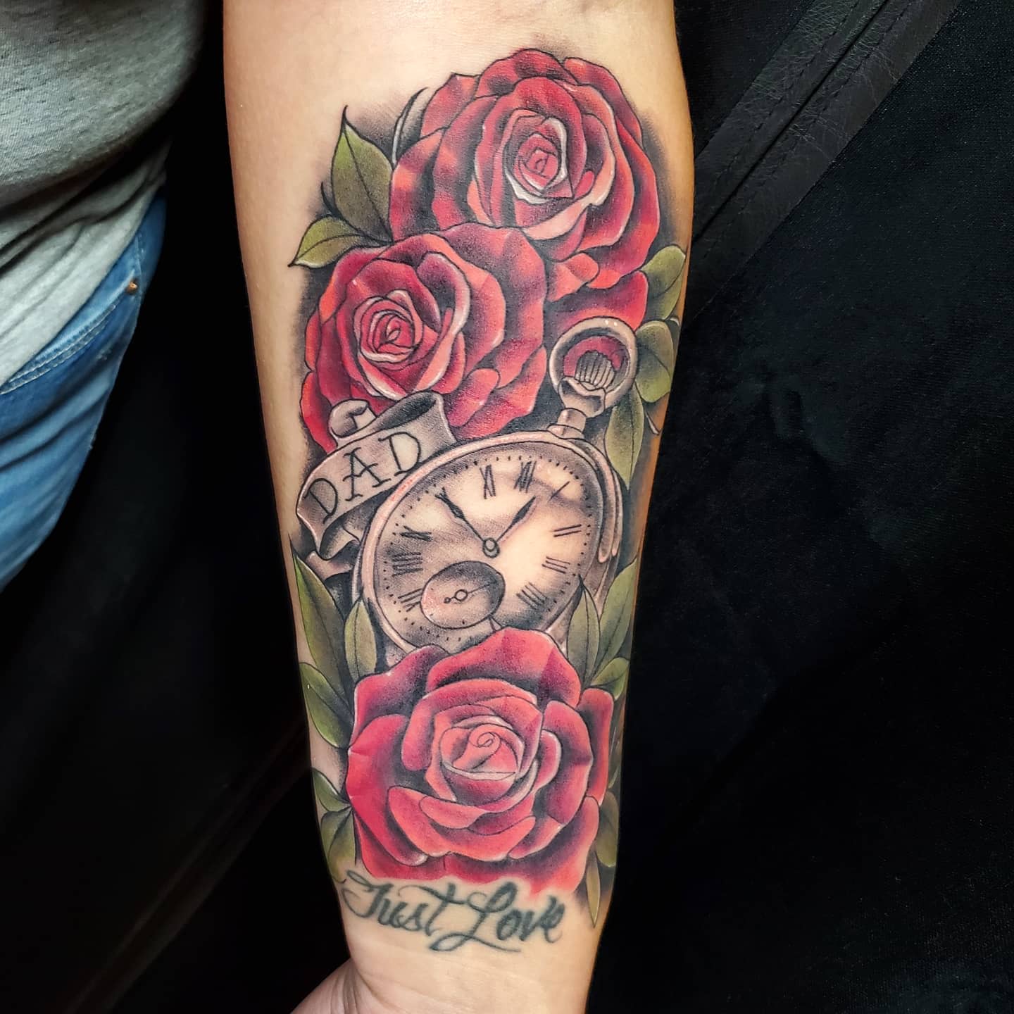 Forearm tattoo of roses, a pocket watch, banner with "Dad," and script "Just Love"