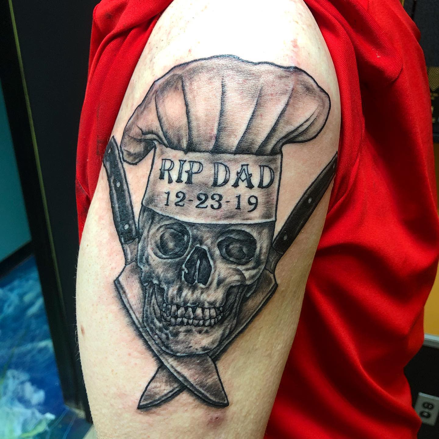 Tattoo of a skull wearing a chef's hat with "RIP DAD 12-23-19" on an upper arm