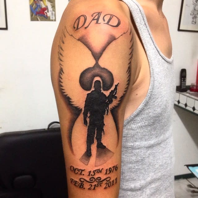 Arm tattoo featuring "DAD," angel wings, soldier silhouette, and birth and death dates