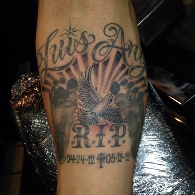 Tattoo of a dove, paw prints, and dates with "Luis Angel" and "R.I.P." on the forearm