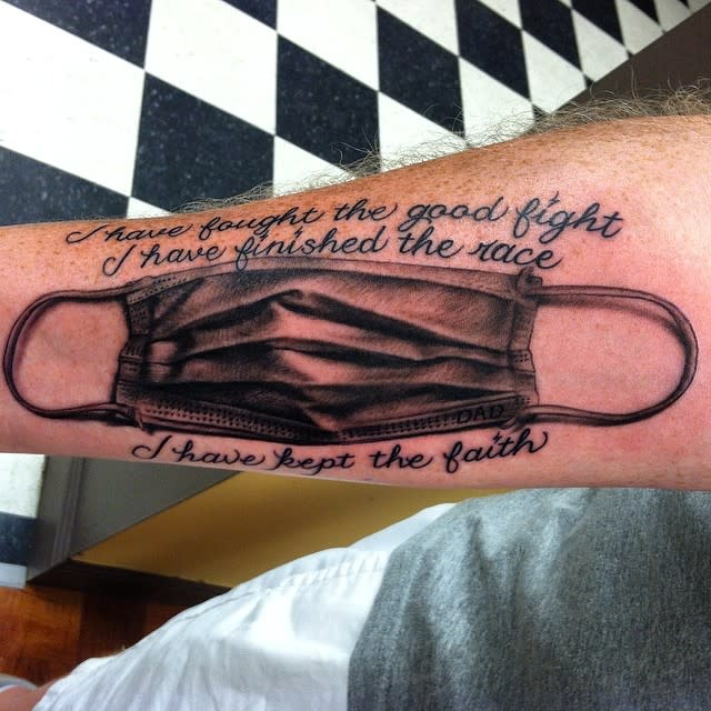 Tattoo of a mask on an arm with the text above and below