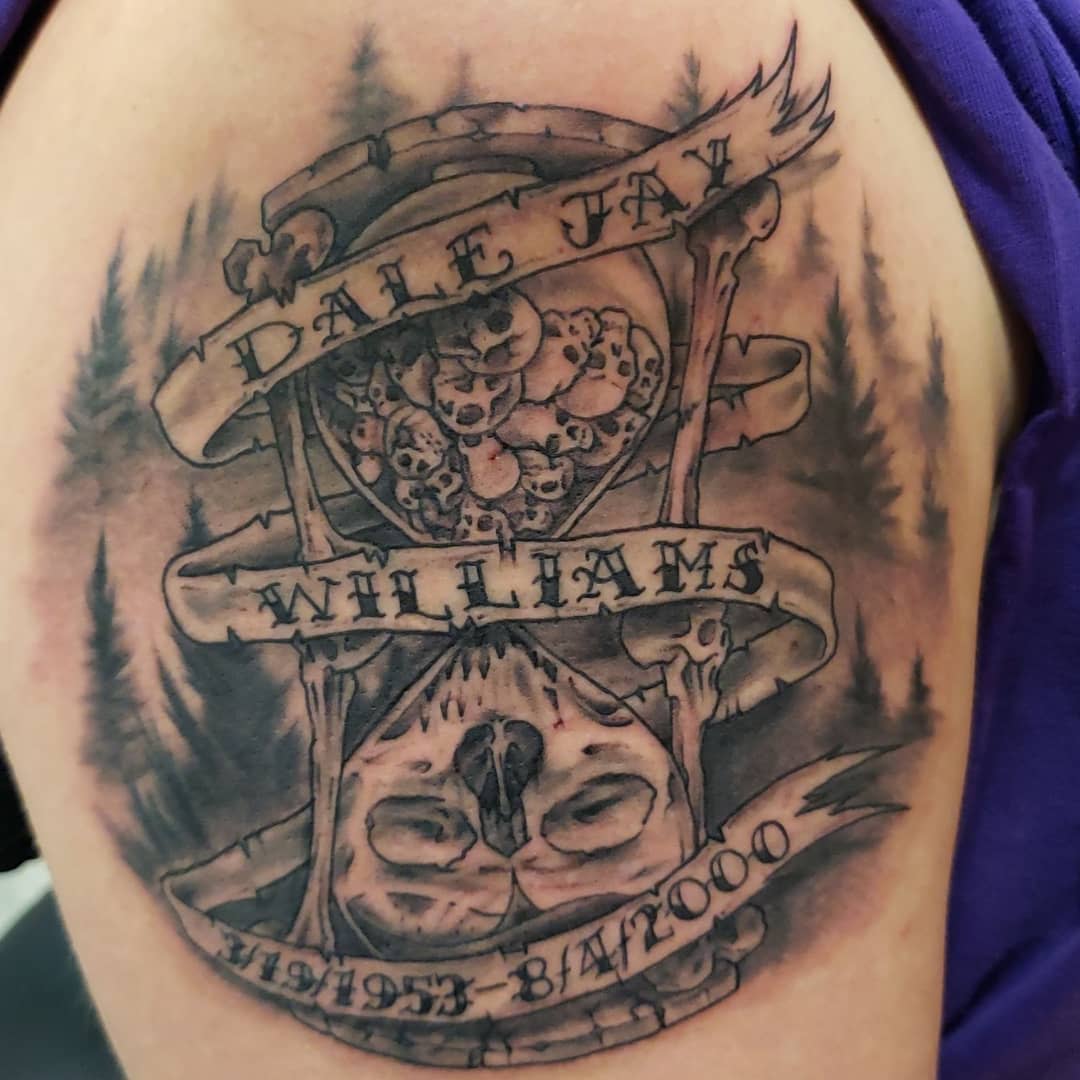 Hourglass tattoo featuring skulls, trees, and script text on upper arm