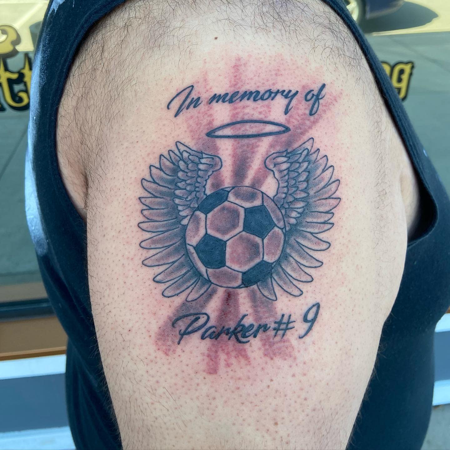 Memorial tattoo of a soccer ball with angel wings and halo, text reads "In memory of Parker #9