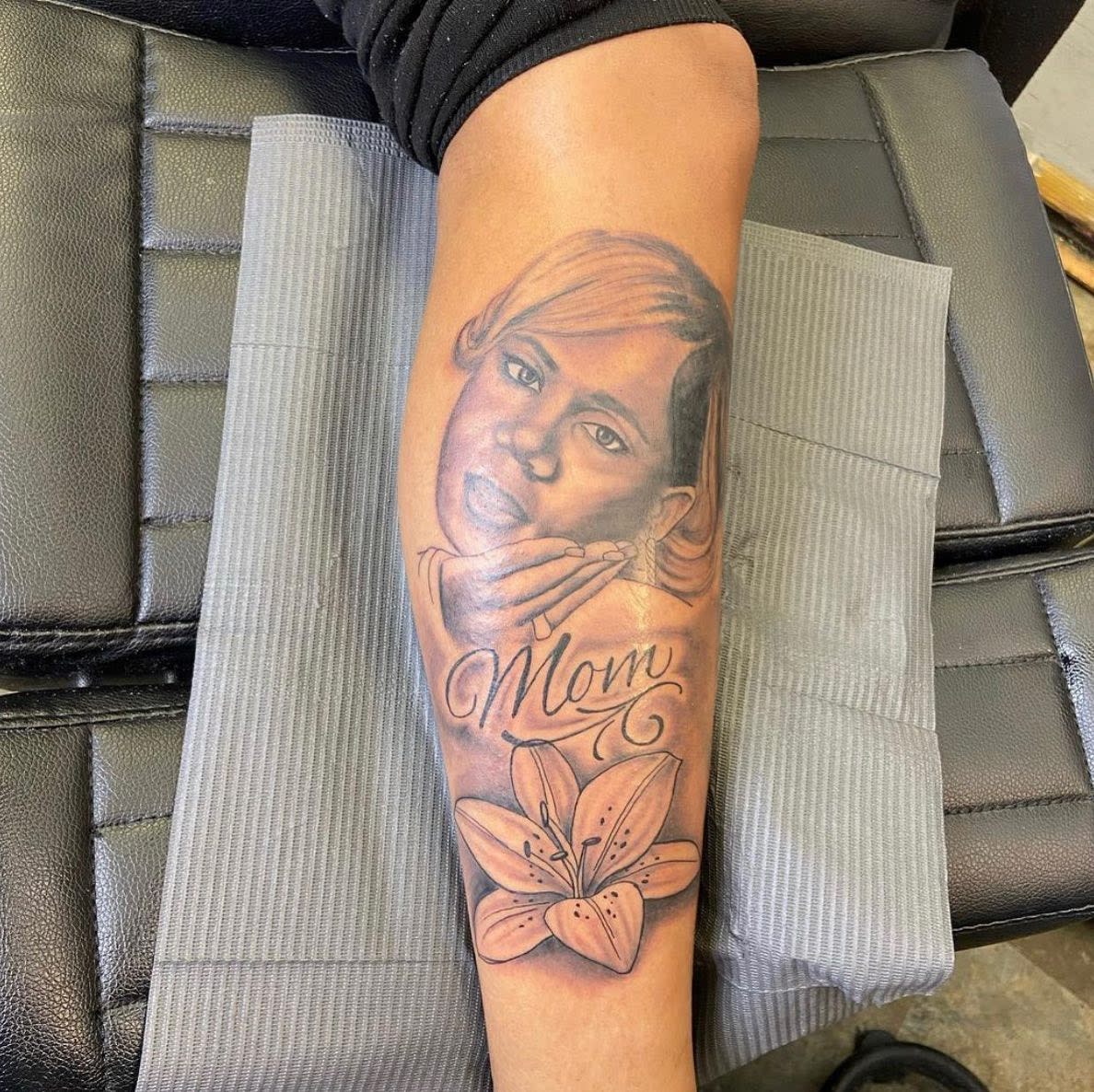 Forearm memorial tattoo of a woman's portrait with the word "Mom" and a flower below it