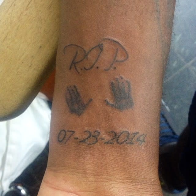 Tattoo on wrist reading "R.I.P." with handprints and date "07-23-2014" below