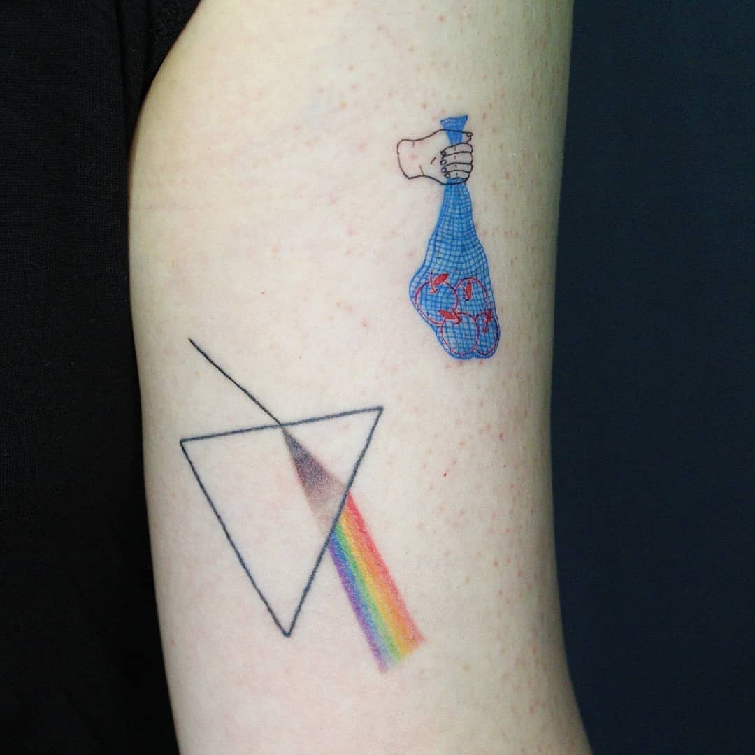 Tattoo of a hand holding a bag of oranges above a prism with a rainbow beam on an arm