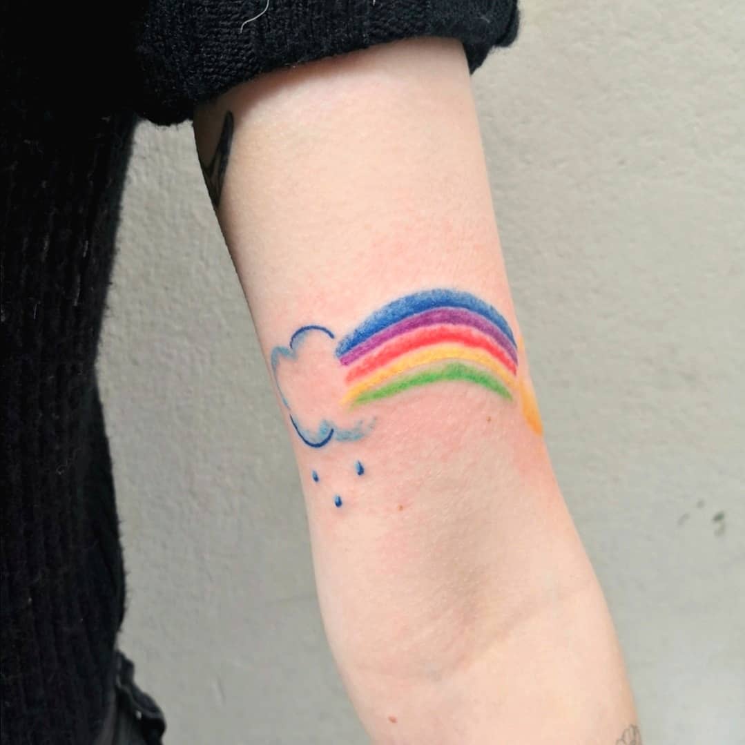 A colorful rainbow tattoo with a cloud and raindrops on an inner arm
