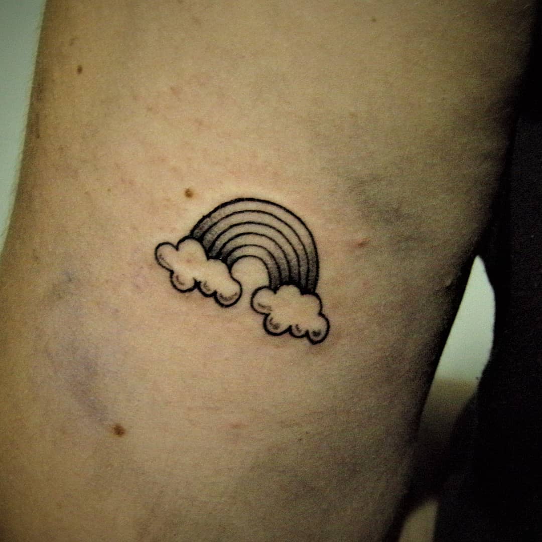 Small outline tattoo of a rainbow emerging from two clouds on an arm