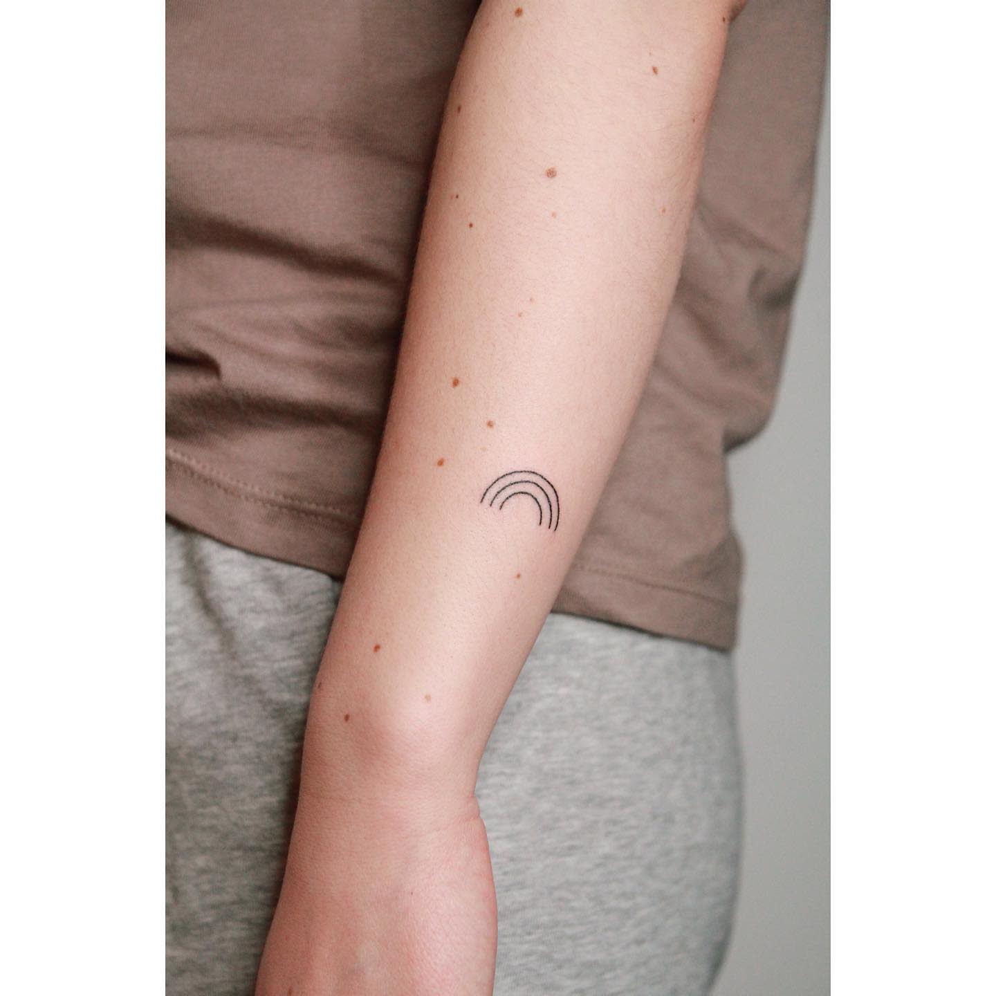 Forearm with a small, black rainbow tattoo on the inner side