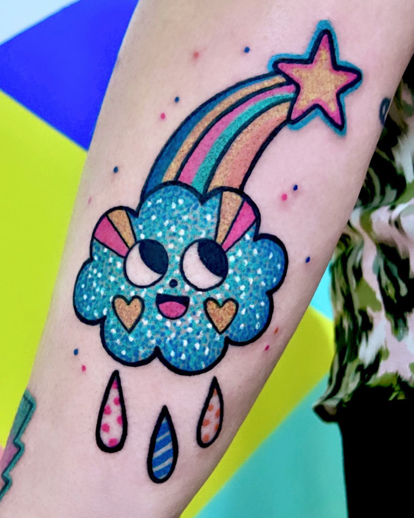 Tattoo of a smiling cloud with rainbow and star, hearts, and colorful raindrops