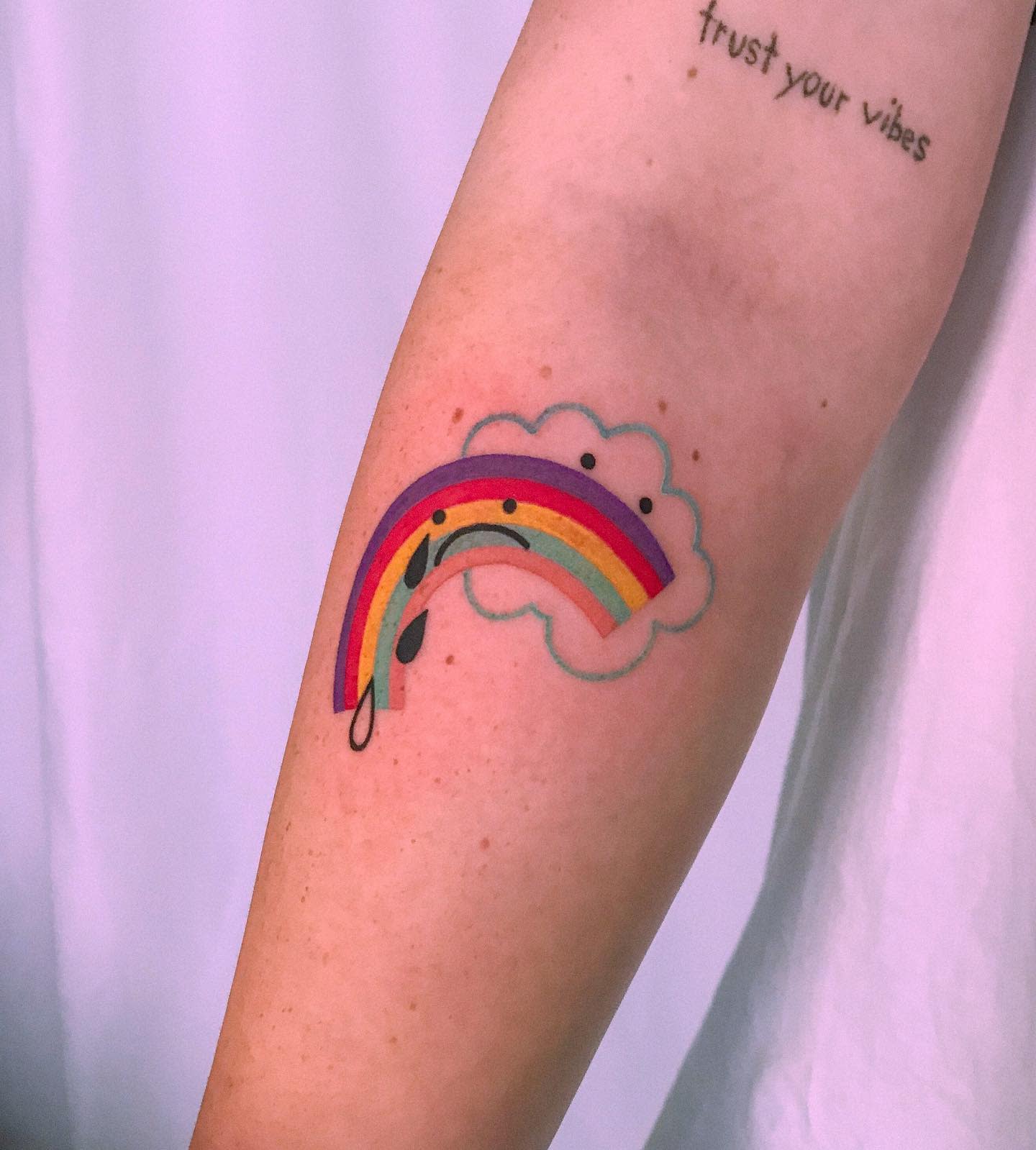 A rainbow tattoo with musical notes on an inner arm that says "trust your vibes"