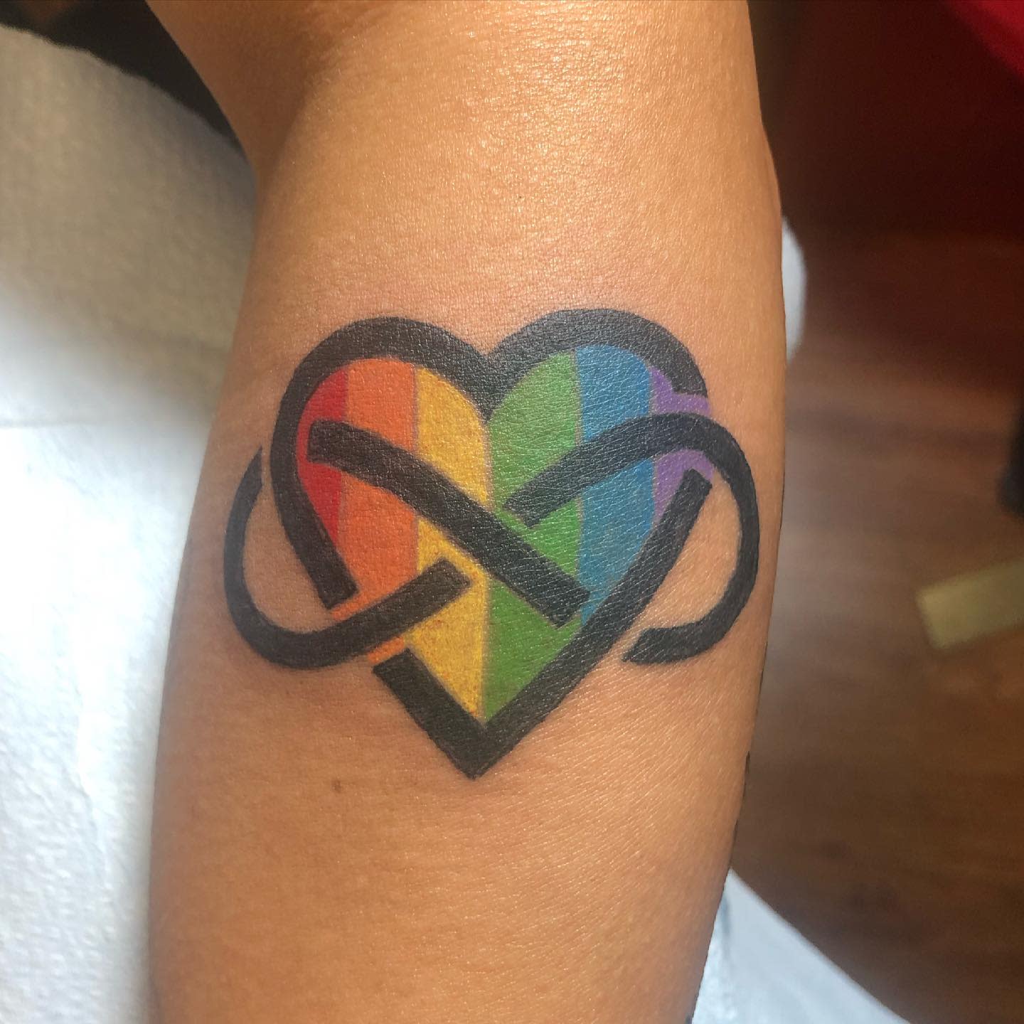 Heart-shaped infinity tattoo with rainbow colors on a forearm