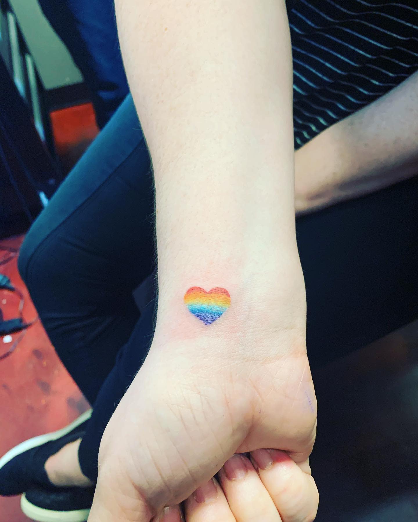 A small heart tattoo in rainbow colors on the inside of a wrist