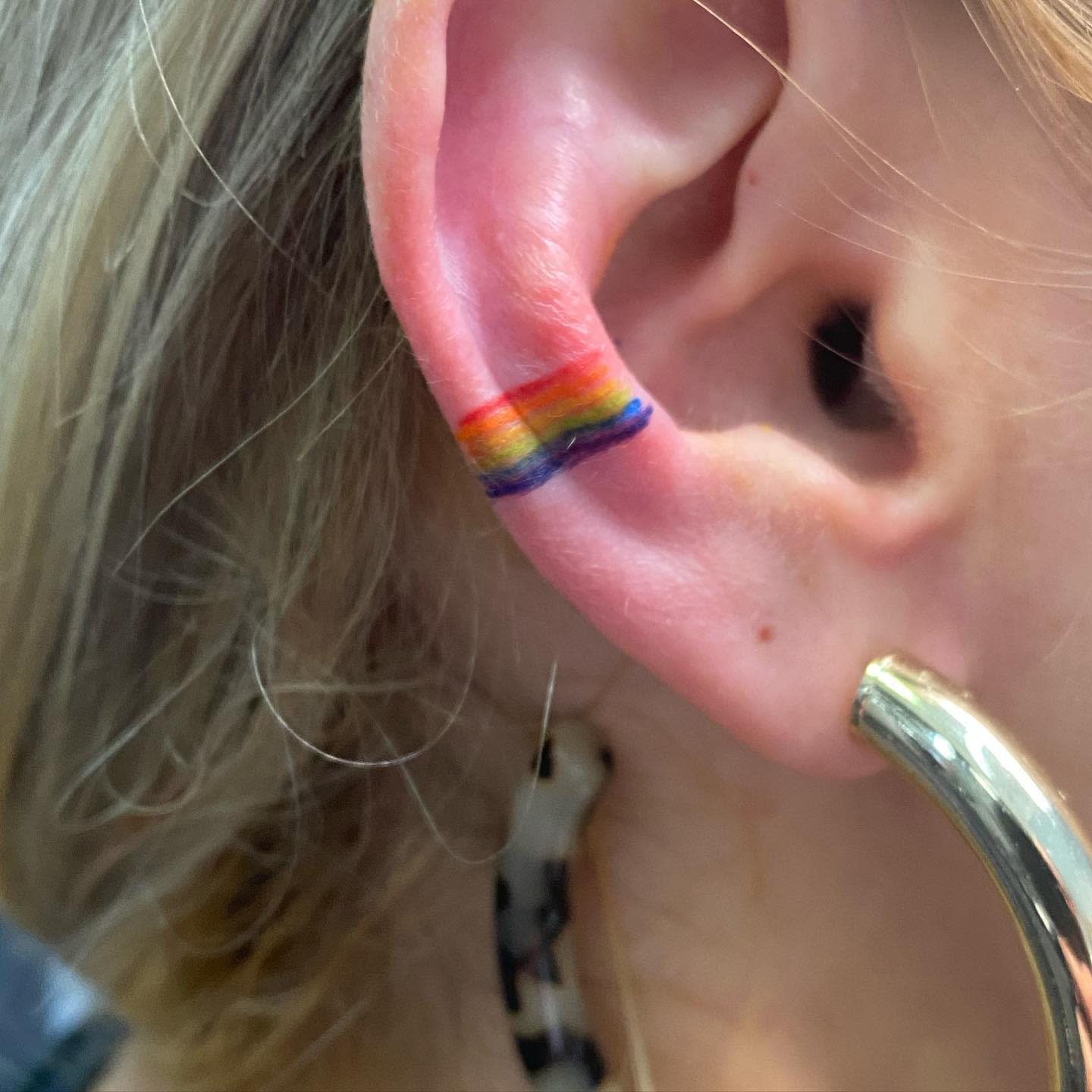 Close-up of an ear with a rainbow-colored tattoo on the inner cartilage