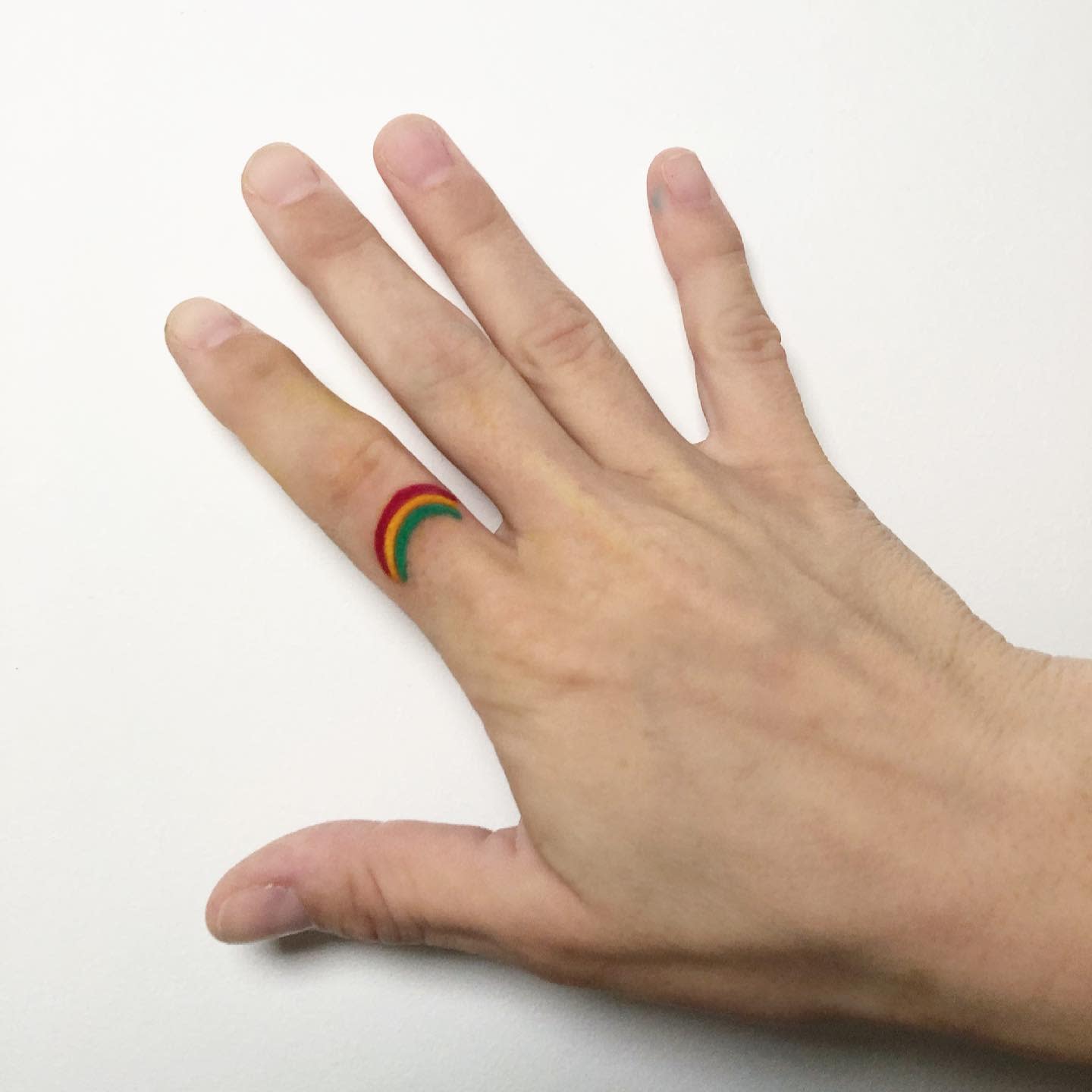 Hand with a rainbow tattoo on the middle finger against a white background