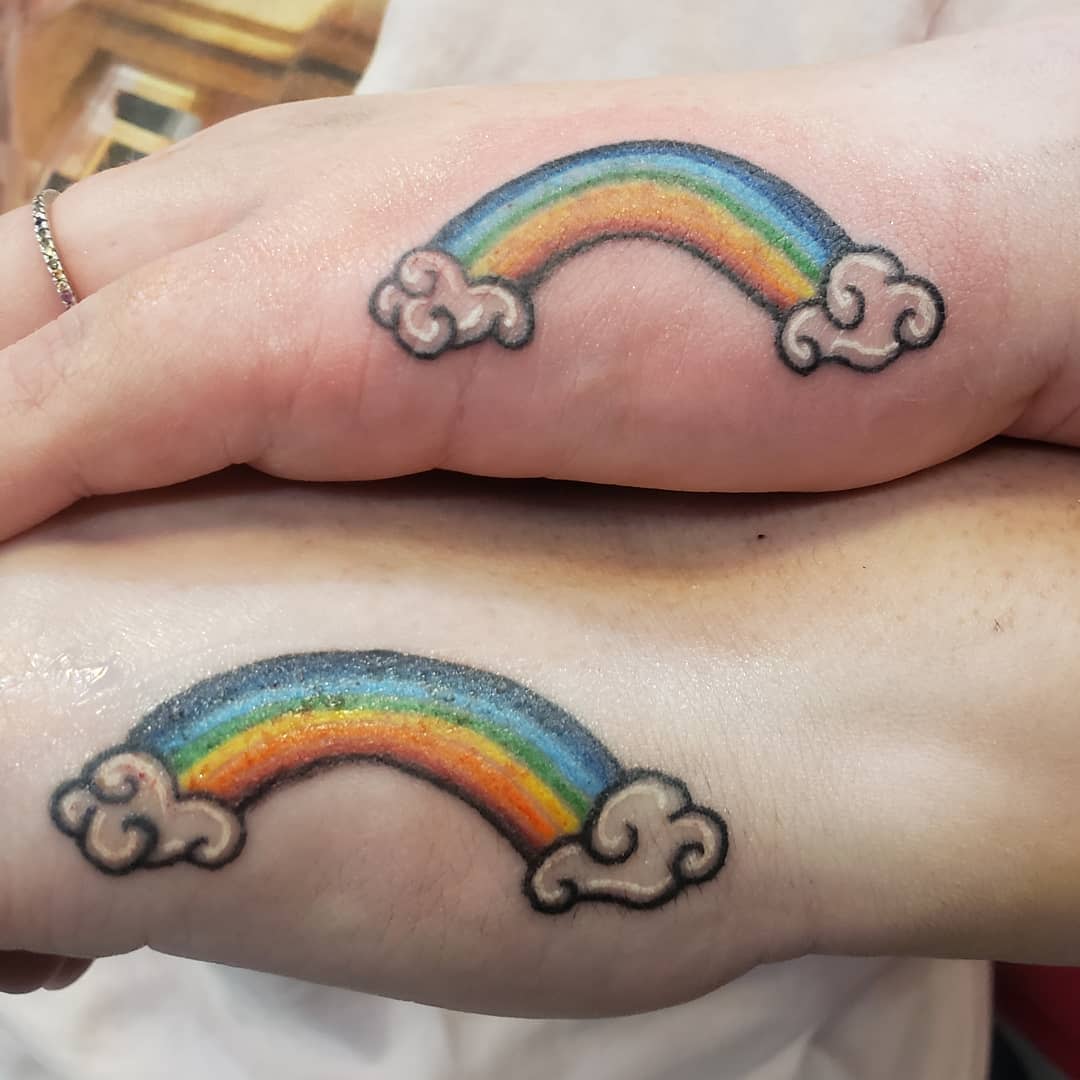 Two matching tattoos of rainbows with clouds on two different wrists