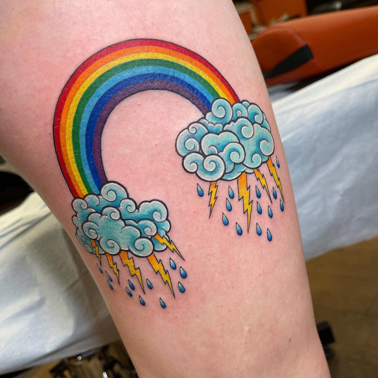 Colorful rainbow tattoo with clouds, lightning bolts, and raindrops on skin