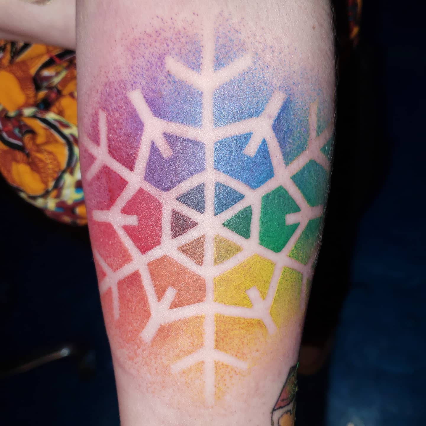 Colorful snowflake tattoo on a forearm with a rainbow gradient background