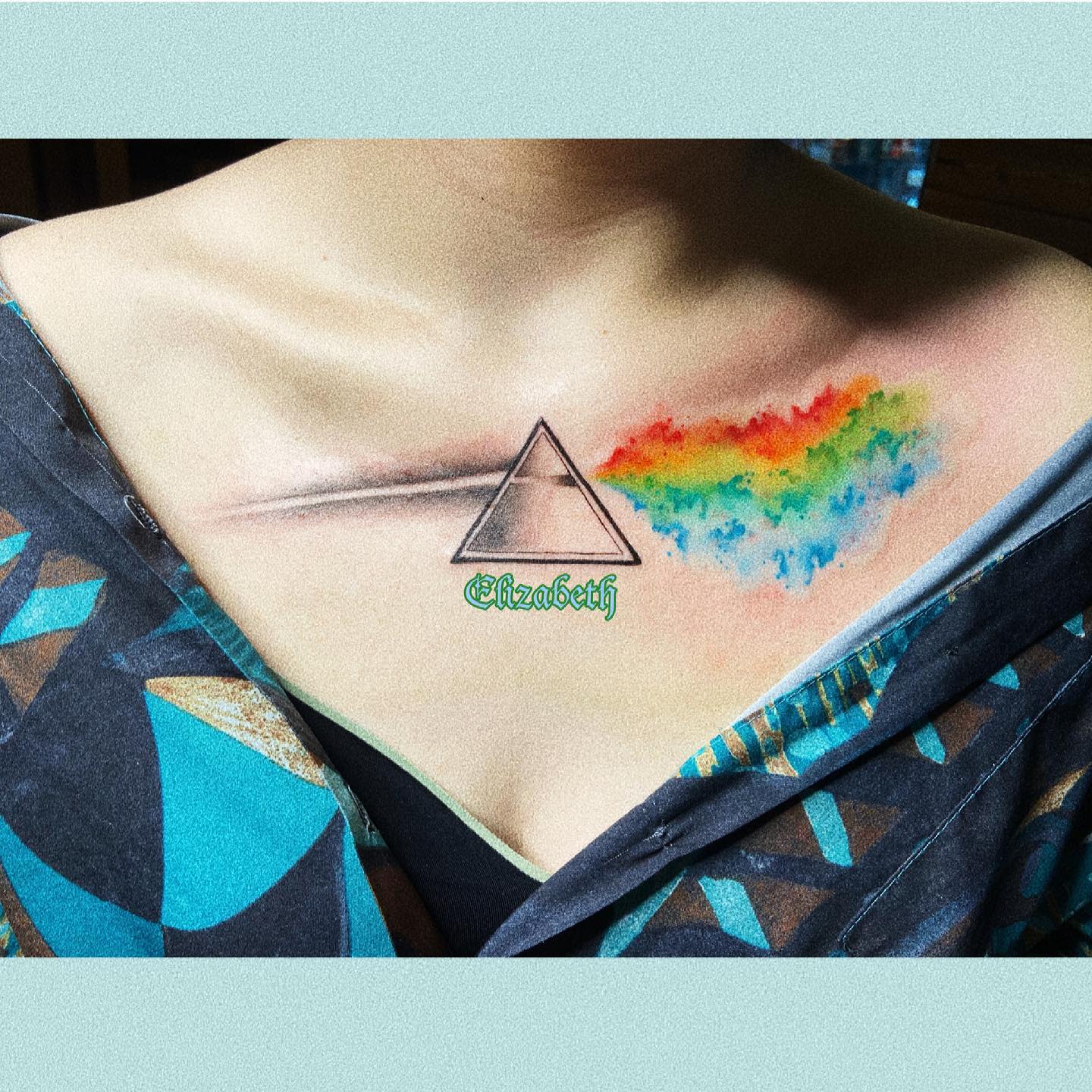 Minimalist tattoo on upper chest featuring a prism and a rainbow splash
