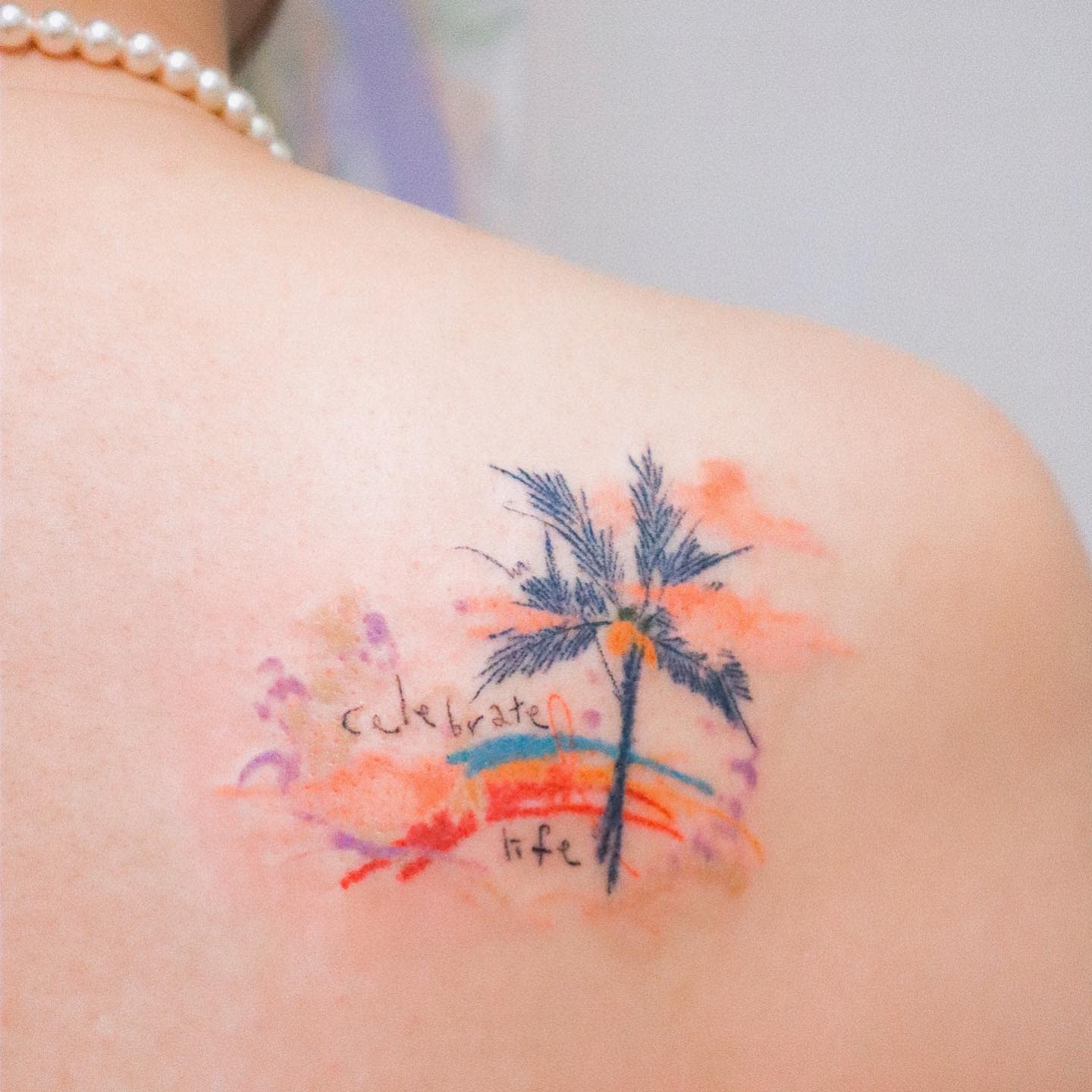 Colorful tattoo of a palm tree and the words "celebrate life" on a shoulder