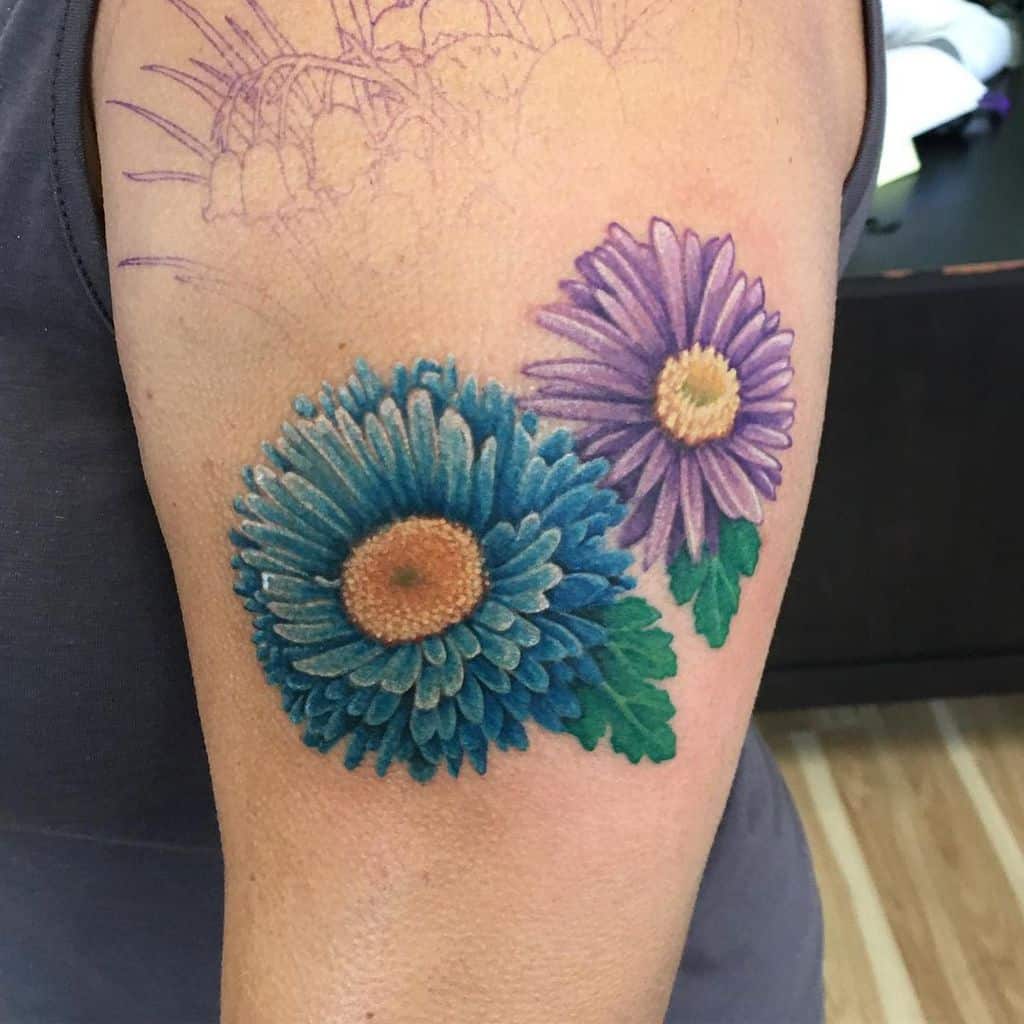 A realistic upper arm tattoo with a blue and purple aster, symbolizing beauty and elegance