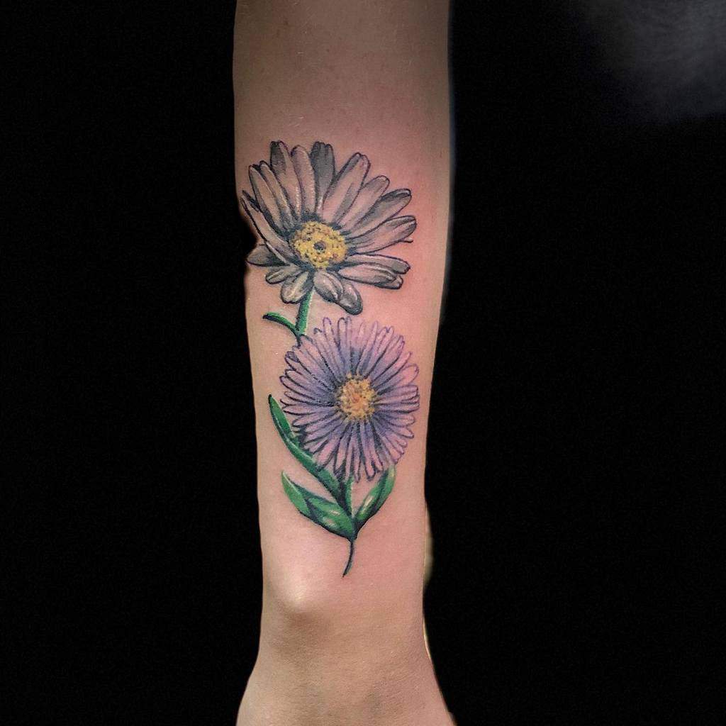 Realistic aster flower tattoo on the forearm, featuring delicate purple petals and green leaves