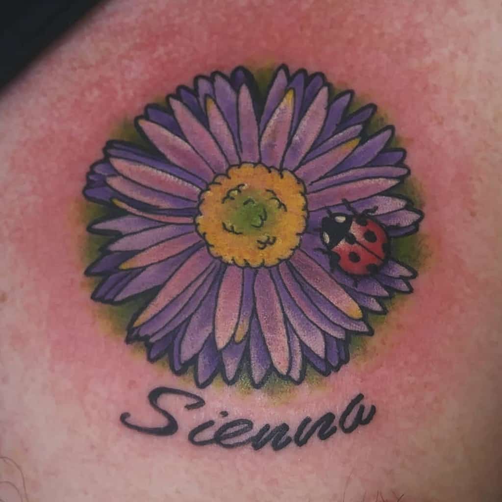 Tattoo of a purple aster with a ladybug and the word "Sienna" underneath