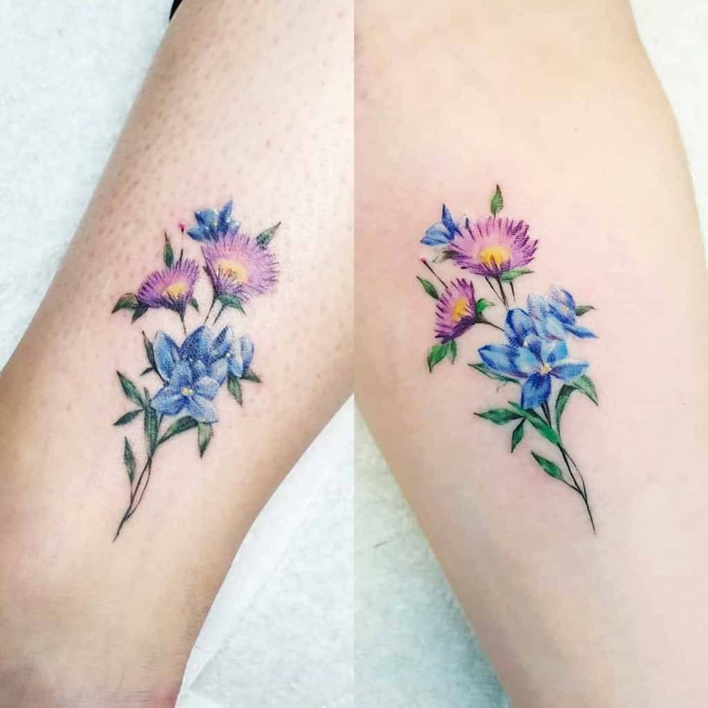 Colorful floral tattoos on two arms featuring stunning purple and blue flowers including delicate asters intertwined with lush green leaves