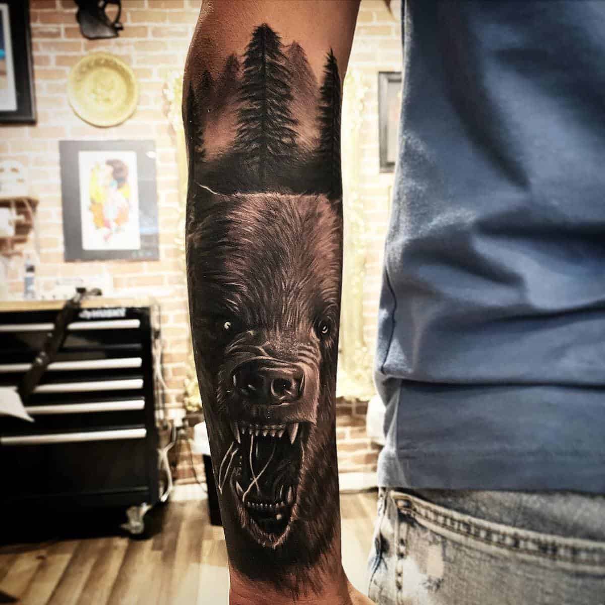 Forearm tattoo of a roaring bear with trees and mountains in the background