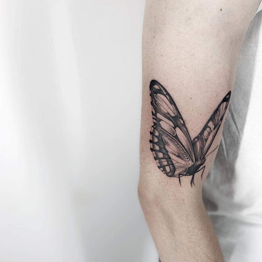 Detailed black butterfly tattoo on a person's upper arm in striking black and white