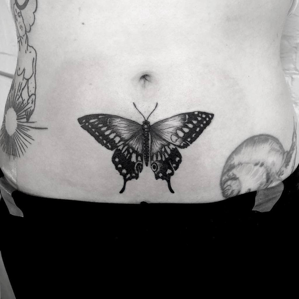 Tattoo of an exquisitely detailed black butterfly on the lower abdomen