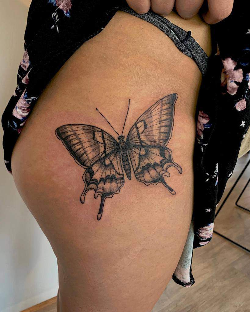 A detailed black butterfly tattoo on a person's upper thigh intricately blends shades of gray for a stunning visual effect