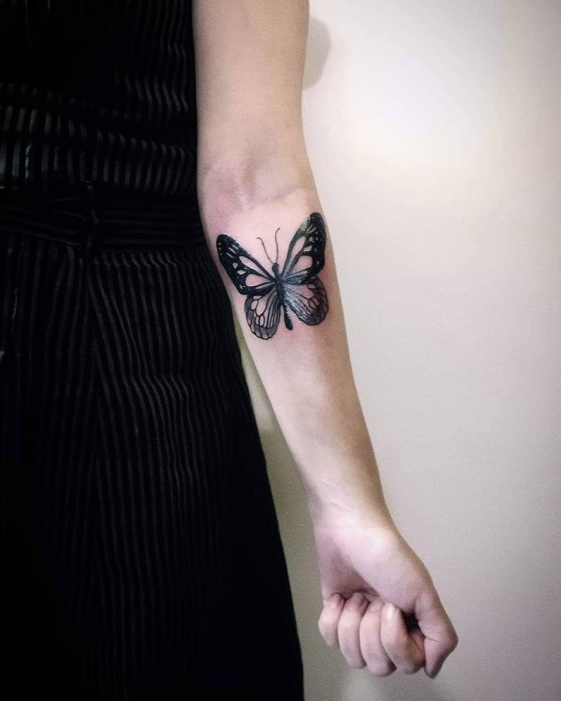 A person proudly displays a black butterfly inked on their inner forearm