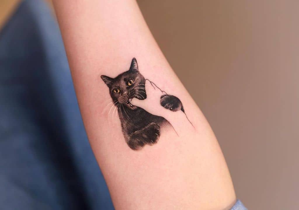 Realistic black cat tatttoo with a playful expression, gently biting and holding a finger in its mouth