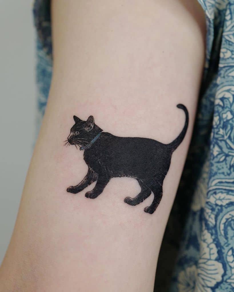 A stylish black cat tattoo adorns the person's upper arm, near the shoulder